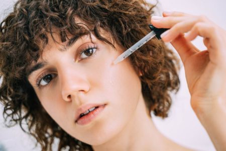 mulher de cabelo cacheado aplicando um produto no rosto