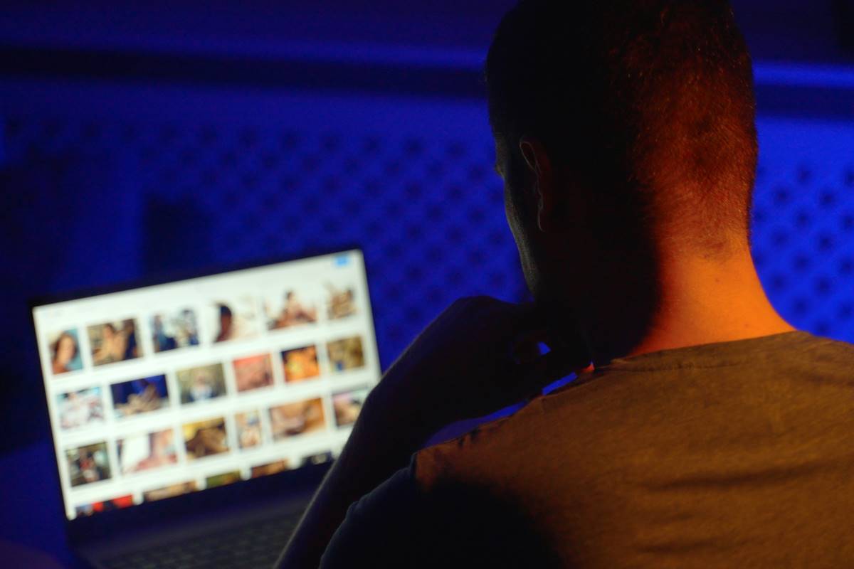 Foto colorida de um homem de costas olhando para a tela do computador no escuro - Metrópoles