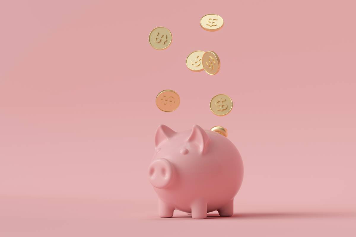 Foto colorida de um cofrinho de porquinho em um fundo cor de rosa com moedas douradas caindo em cima - Metrópoles