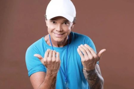 Cantor Netinho posa de blusa azul e boné branco - Metrópoles