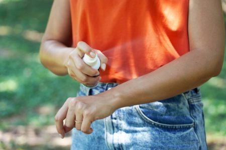 Mulher de blusa laranja aplica repelente no braço - Metrópoles