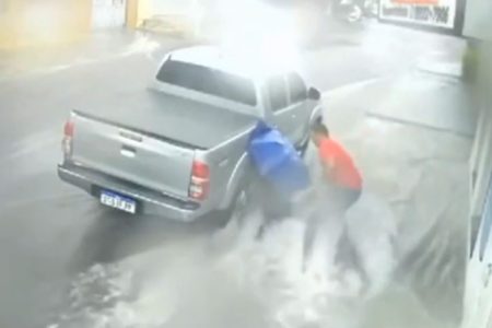 Imagem colorida mostra comerciante indo socorrer mulher que caiu e foi arrastada pela correnteza causada por uma forte chuva - Metrópoles