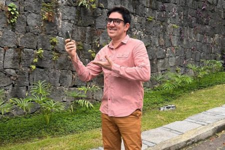 Foto colorida de Marcelo Adnet com blusa rosa e calça marrom - Metrópoles