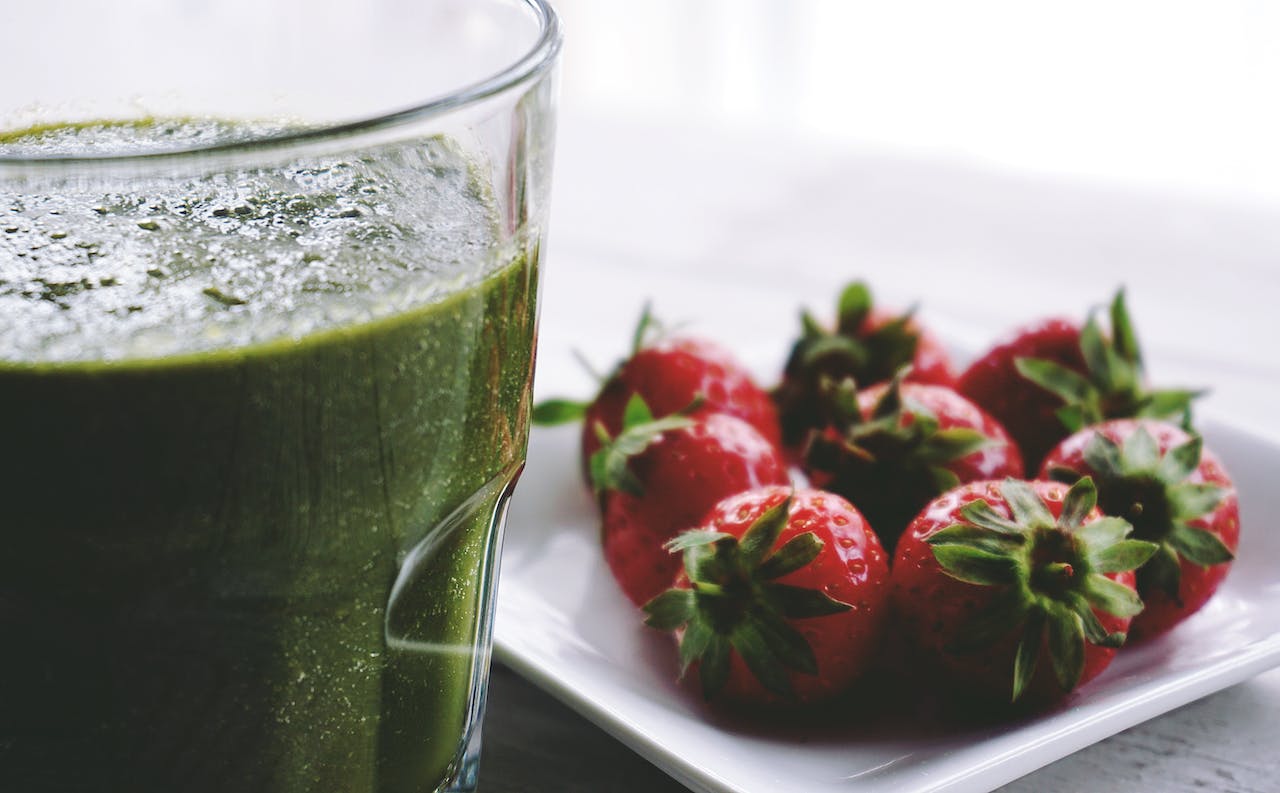 Copo com suco verde e morangos ao fundo - Metrópoles
