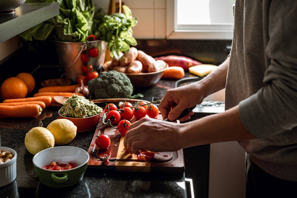 Moça cortando tomate com diversos alimentos na bancada