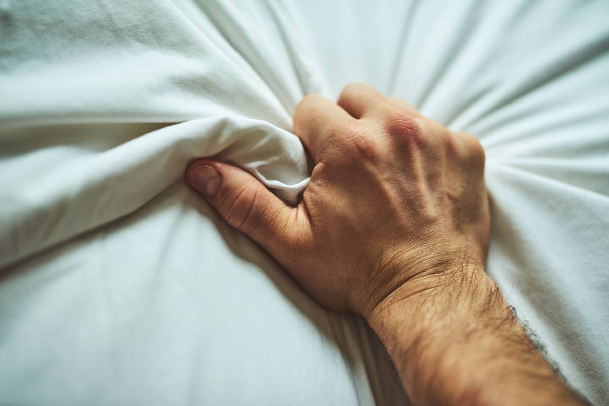 Foto colorida de uma mão masculina apertando um lençol branco em close - Metrópoles