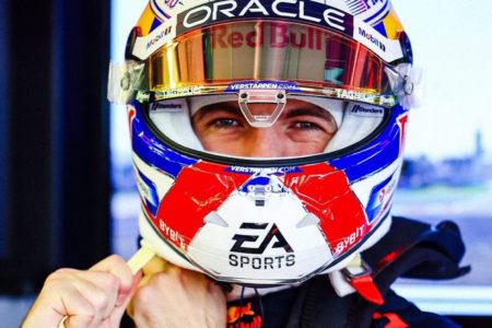 Imagem colorida mostra o piloto Max Verstappen afivelando o capacete