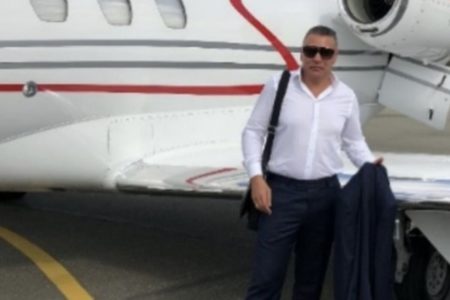 Foto colorida mostra homem com camisa branca, dentro de calça jeans, em frente a avião de pequeno porte - Metrópoles