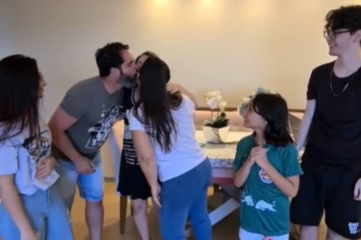 Foto colorida de um trisal se beijando e três filhos olhando - Metrópoles