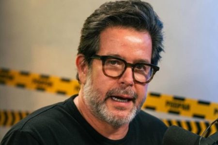 Foto colorida de Murilo Benício. Ele está falando, usa óculos com armação preta, tem cabelo preto, barba grisalha e usa camisa preta - Metrópoles