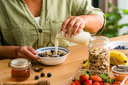 mulher adicionando leite a um bowl com cereais e frutas