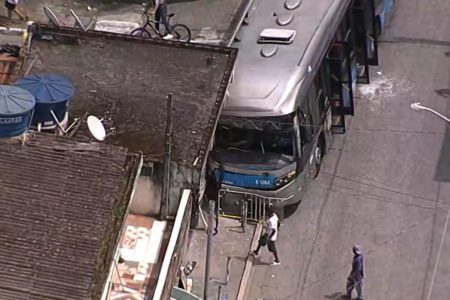 Print de cena de acidente. Ônibus está parado com as portas abertas após bater contra parede externa de estabelecimento comercial.