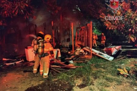 Foto colorida tirada à noite de quatro bombeiros em meios à escombros carbonizados