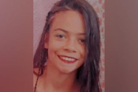 Rosto de adolescente com cabelos escuros sobre parte do lado direito do rosto. Ela tem olhos escuros e sorri.