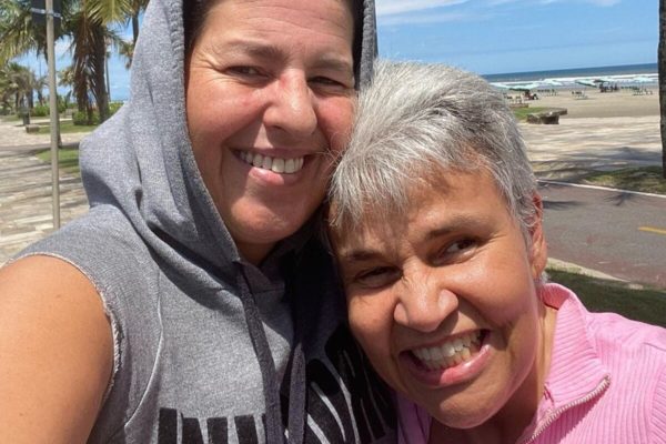 Claudia Rodrigues e a namorada Adriane Bonato posam juntas e sorridentes - Metrópoles