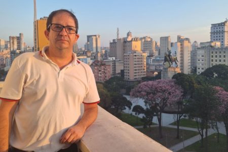 imagem colorida mostra homem branco, de óculos de grau e camisa polo branca em varada de apartamento. ao fundo está a praça princesa isabel - metrópoles