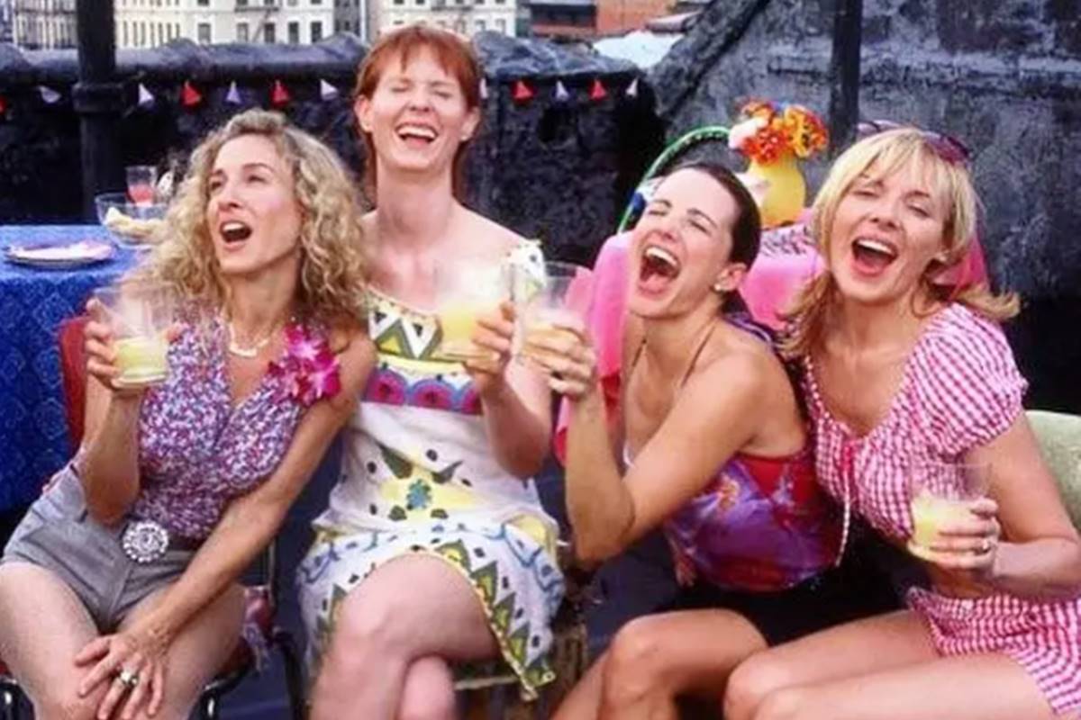 Foto colorida de quatro mulheres rindo com copos na mão - Metrópoles