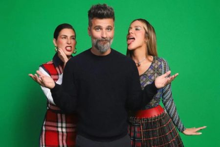 Na imagem colorida, homem e duas mulheres aparecem em fundo verde. Os três fazem caras e bocas e usam roupas coloridas - Metrópoles