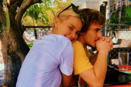 Na imagem colorida, mulher de blusa branca abraça rapaz de roupa amarela. Os dois estão sentados em uma mesa, em um jardim - Metrópoles