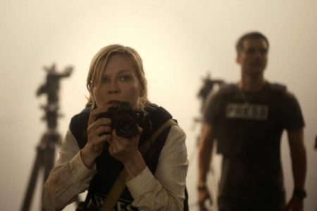 foto colorida de mulher com camera fotografica e wagner moura ao fundo embaçado - metrópoles