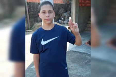 Imagem de menino branco, com camiseta preta, fazendo gesto com a mão esquerda - Metrópoles