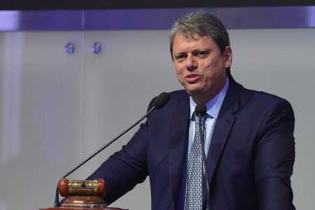 Imagem colorida mostra Tarcísio de Freitas, homem branco, grisalho, vestindo terno e gravata, em um púlpito com dois microfones finos, falando de forma sorridente ao aprovar novo salário mínimo paulista - Metrópoles