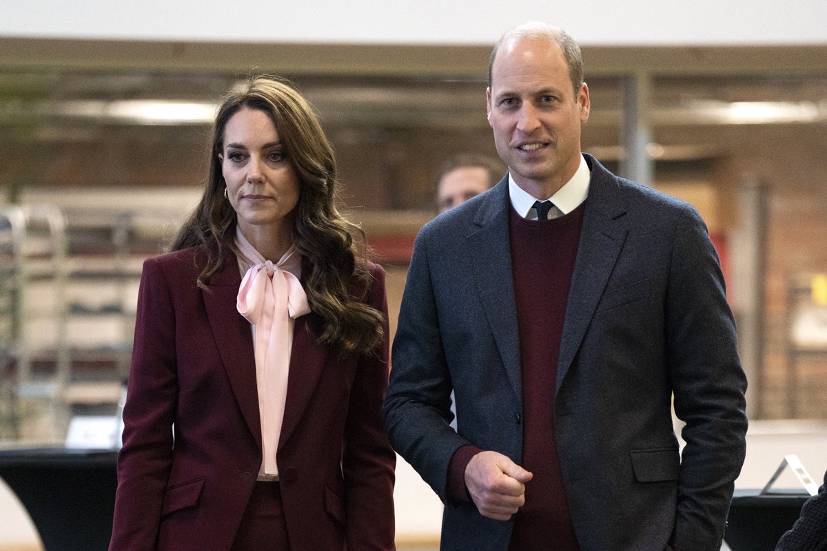 Foto colorida de mulher com roupa vinho e rosa. Ao lado dela, está um homem com blazer preto e blusa na cor vinho - Metrópoles
