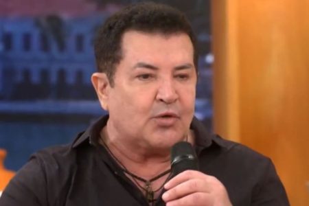 Foto colorida do cantor Beto Barbosa. Ele fala com um microfone na mão e usa camisa de botão preta - Metrópoles