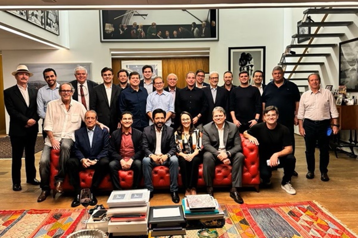 Imagem colorida mostra grupo de homens brancos, todos vestindo terno, na sala de uma mansão - Metrópoles