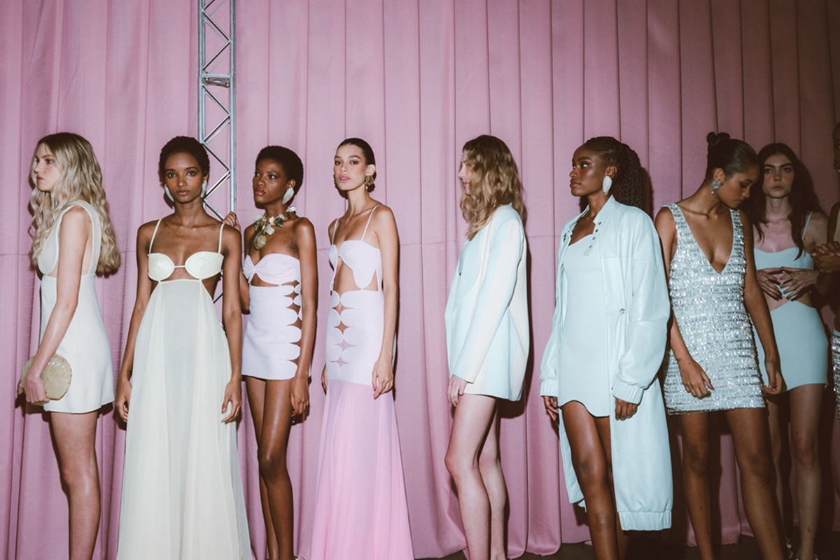 Na imagem com cor de fundo rosa, modelos estão enfileiradas usando looks claros - Metrópoles
