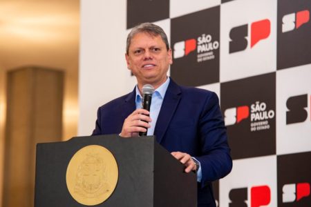 Imagem colorida mostra Tarcísio de Freitas em um púlpito com logotipo do governo de SP e um banner ao fundo - Metrópoles