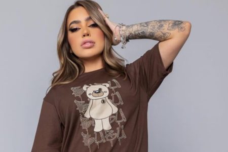 MC Mirella posa com um blusão marrom, com estampa de urso, e a mão na cabeça - Metrópoles