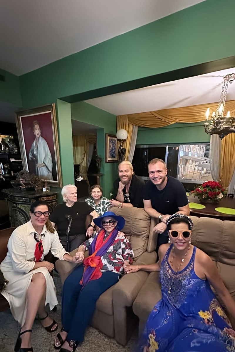 Foto colorida de pessoas posando para uma fotografia. Eles estão em uma sala com obras de arte - Metrópoles