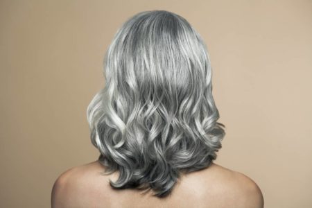 Foto colorida de uma mulher branca de cabelo grisalho de costas em um fundo bege - Metrópoles