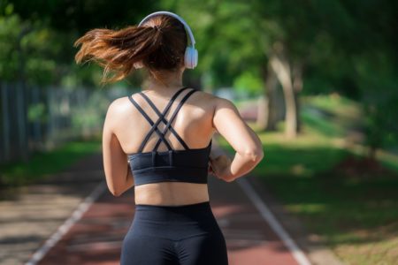 Imagem mostra mulher branca de top e calça preta e fones de ouvido correndo - Metrópoles