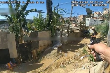 Frame de vídeo. Imagem mostra PM apontando arma para homem de costas antes de disparar - Metrópoles