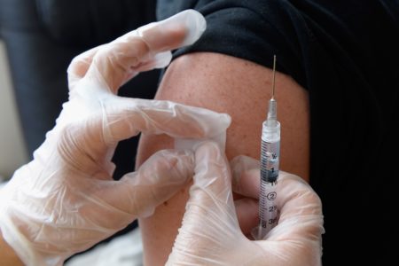 Mãos com luvas médicas seguram seringa de vacina e aplicam curativo em braço