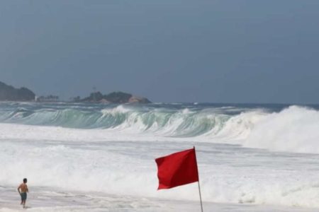 foto colorida de ondas em praia, com bandeira vermelha de alerta - Metrópoles