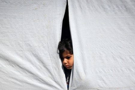 Foto colorida de um menino que olha de dentro de uma tenda em Rafah, no sul da Faixa de Gaza - Metrópoles