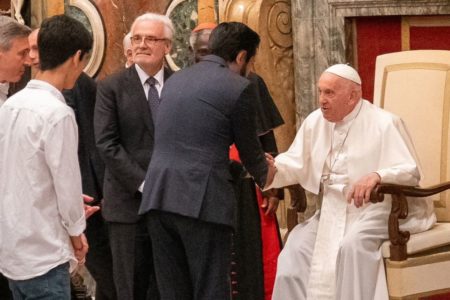 Foto colorida do prefeito de São Paulo, Ricardo Nunes, de terno escuro e de costas, cumprimentando o Papa Francisco, de branco e sentado - Metrópoles