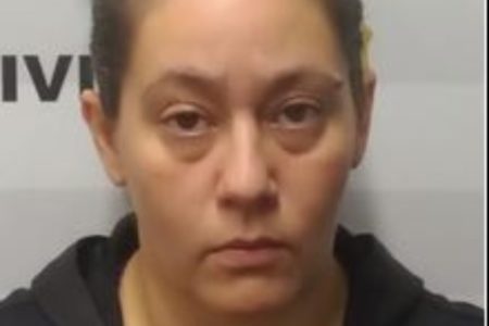 Foto colorida de mulher branca, com semblante sério, em frente paredão de delegacia - Metrópoles