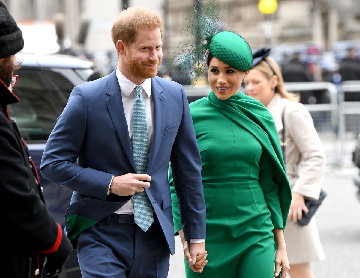 Foto colorida de homem ruivo com terno azul e mulher com roupa verde. Eles estão caminhando - Metrópoles