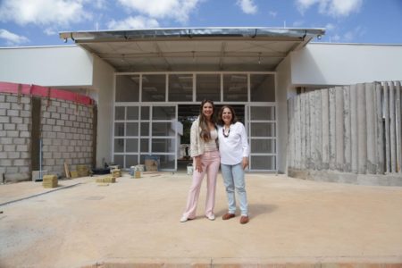 Foto colorida de deputada e reitora da unb sorrido para foto em frente à prédio em obra