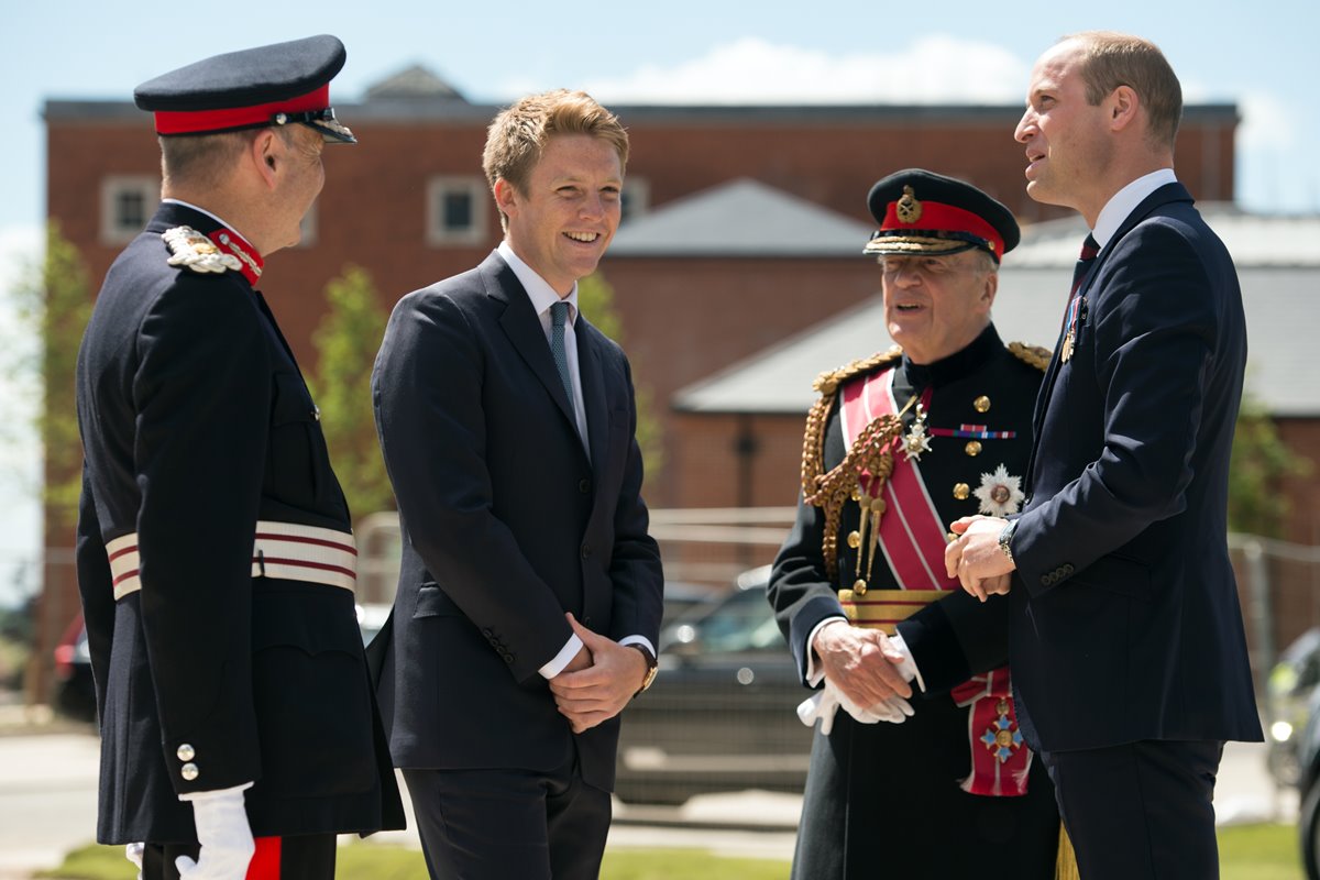 Foto colorida de quatro homens, sendo dois com terno e dois com roupas militares britânicas - Metrópoles