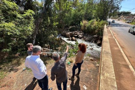 Foto colorida de pessoas de roupa social ao lado de ponte sob córrego