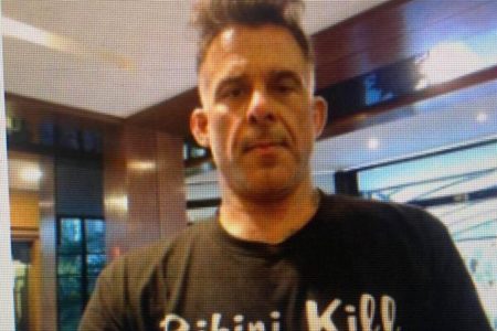 Homem branco sem barba e cabelo curto usando camiseta preta com os dizeres "bikini kill" - Metrópoles