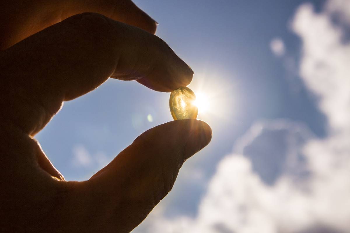 Foto colorida - Mão segurando um comprimido na frente do sol - vitamina d