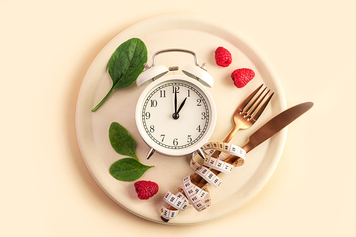 Composição de alimentos saudáveis com talheres, prato, fita métrica, framboesas vermelhas frescas e despertador em fundo bege pastel, Close-up