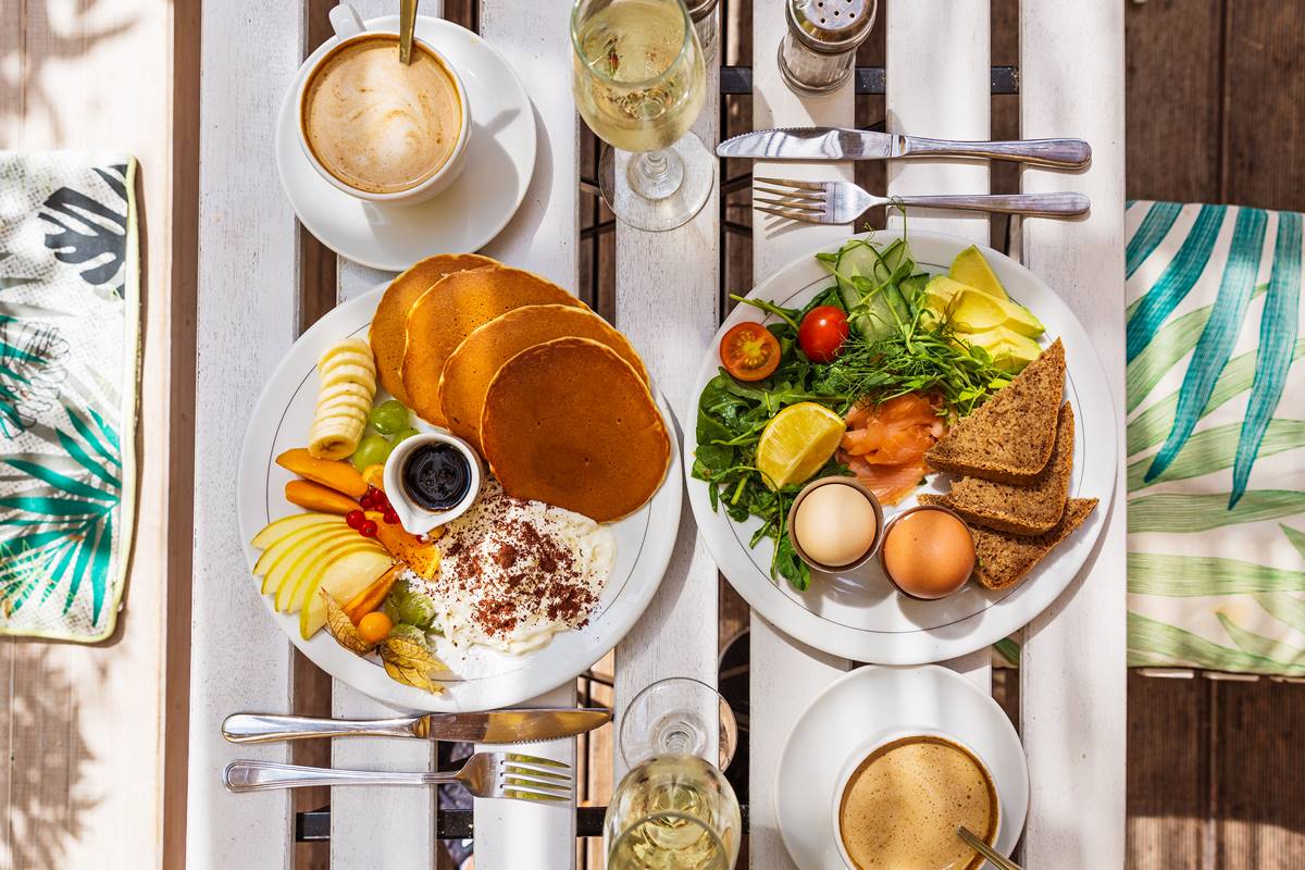 Foto colorida - Mesa de café da manhã com dois pratos, com ovos, pães, panquecas e frutas