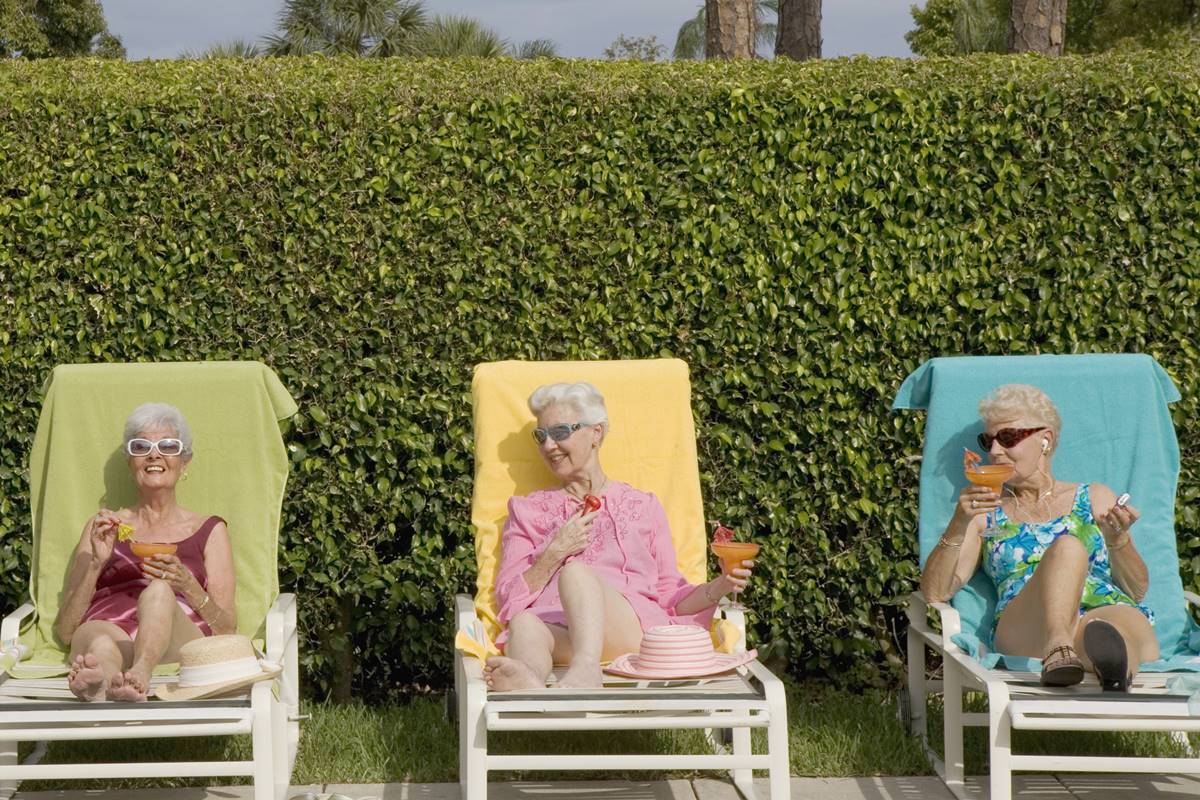 Foto colorida de mulheres sentadas em espreguiçadeiras em um jardim. Elas tomam drinques - Metrópoles